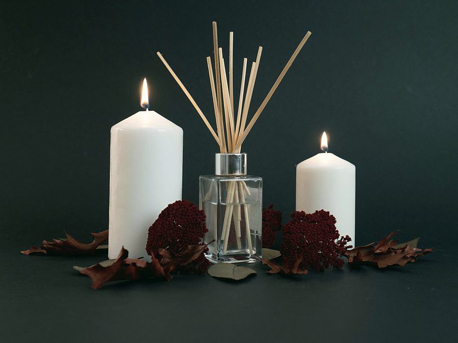 Lit pillar candles and a reed diffuser with autumn botanicals